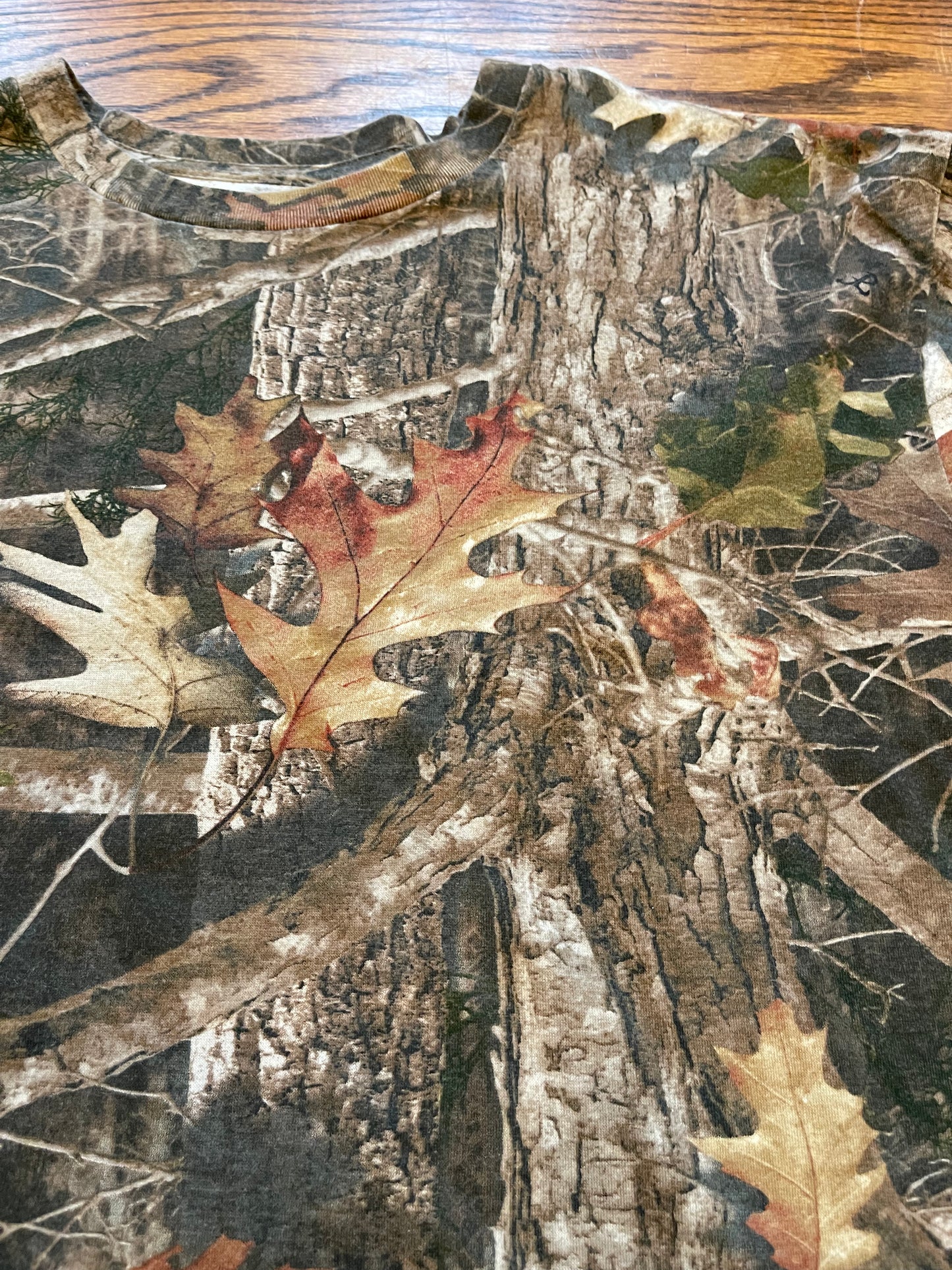 Camouflage pattern with tree bark, leaves, and branches on a wooden surface