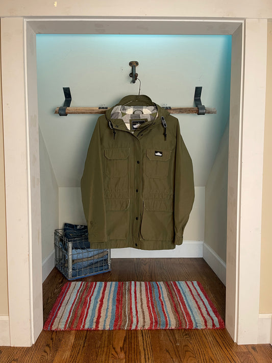 Green jacket hanging on a rack in a room with a striped rug on the floor.