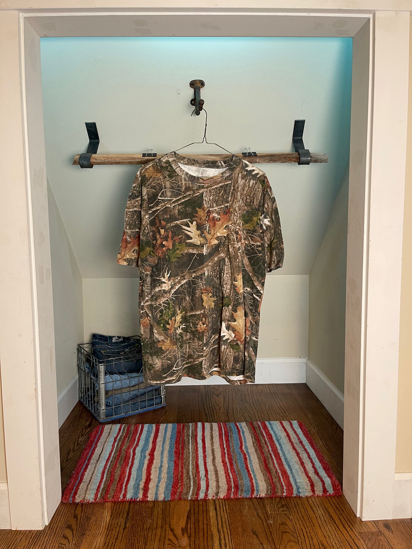 front view camouflage shirt hanging on a rack in a room with a striped rug on the floor.