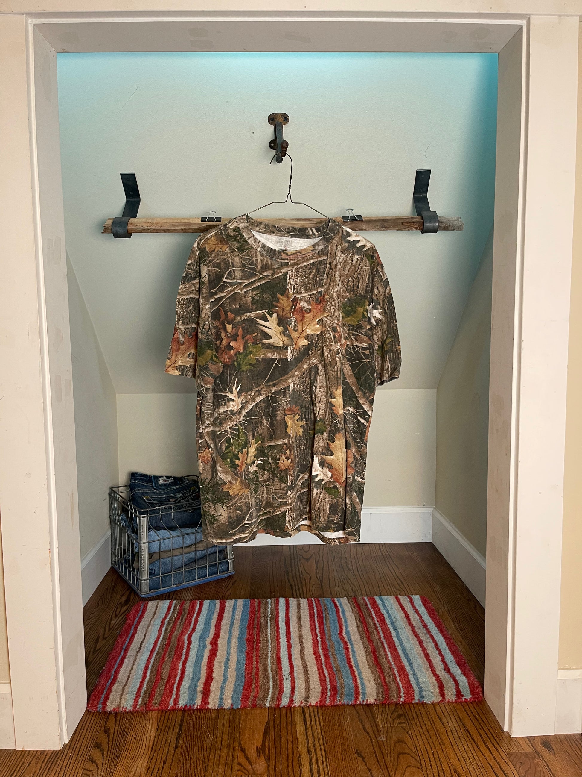 front view camouflage shirt hanging on a rack in a room with a striped rug on the floor.