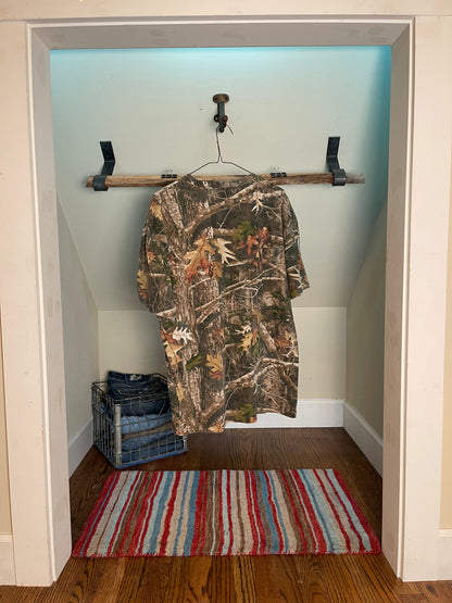 Back view camo-patterned shirt hanging on a rack in a room with a striped rug.